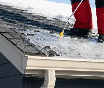 Ice dam removal technician using a steam wand to melt thick ice buildup on a residential roof in {city}, {state}